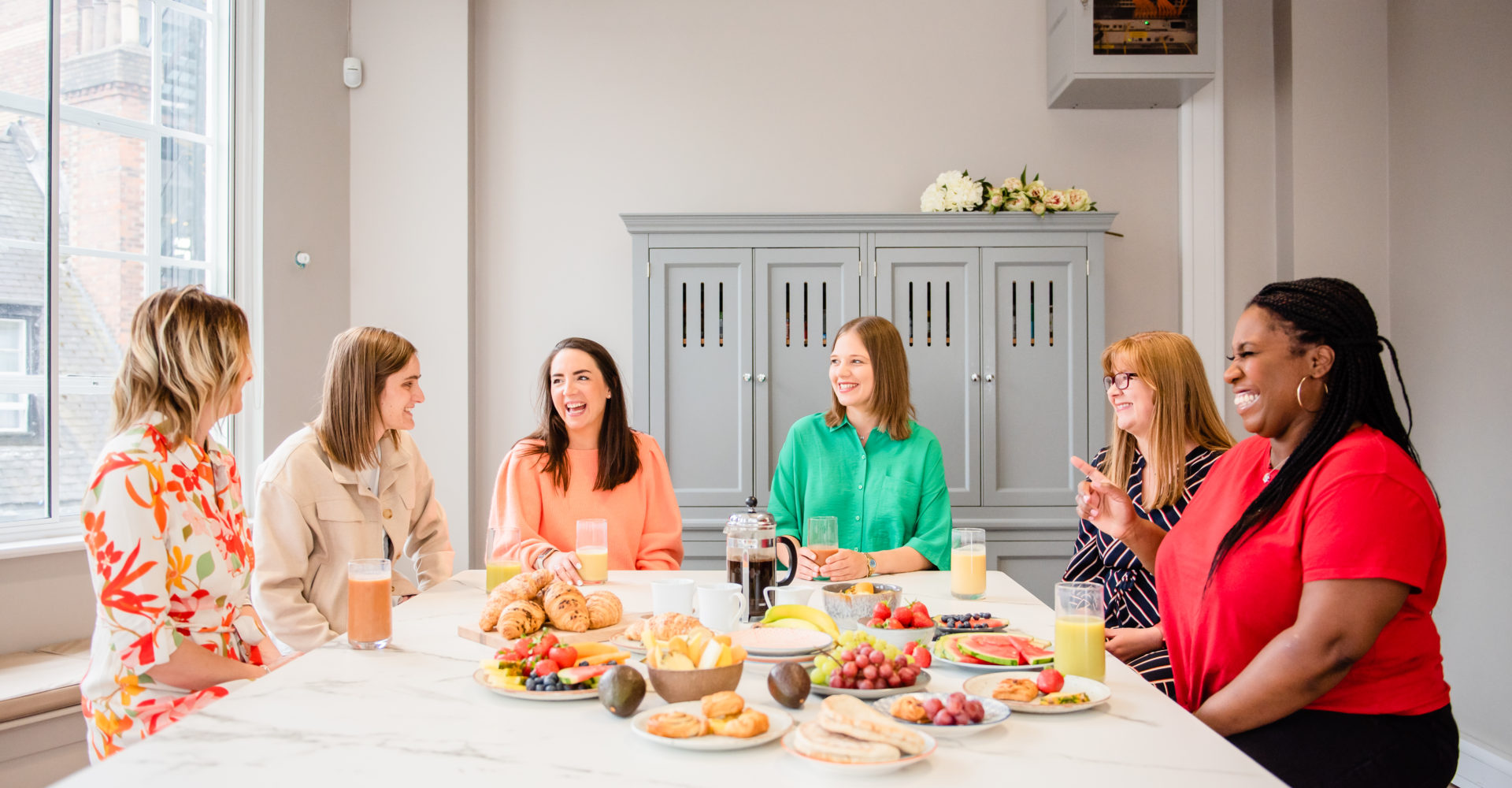 6 people sat round a table, discussing topics. With a selection of foods on the table